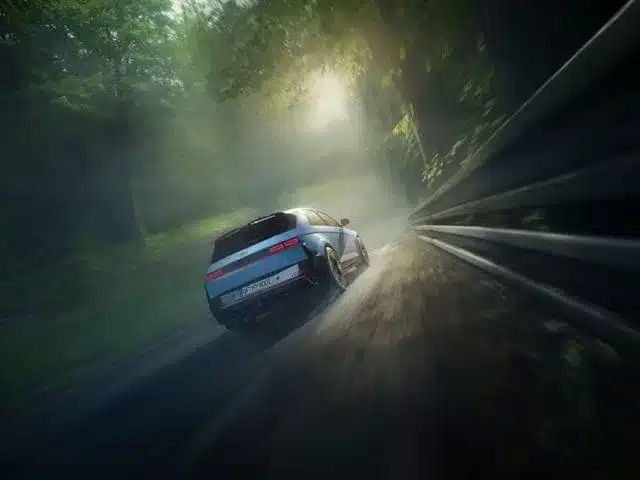 Hyundai IONIQ 5 N fährt sportlich auf einer kurvigen, vom Licht durchfluteten Straße durch den Wald.