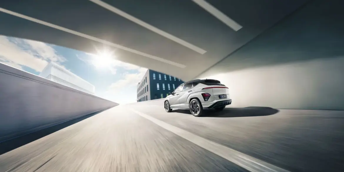 Heckansicht eines weißen Hyundai KONA Elektro, der auf einer städtischen Straße unter einer Brücke fährt.