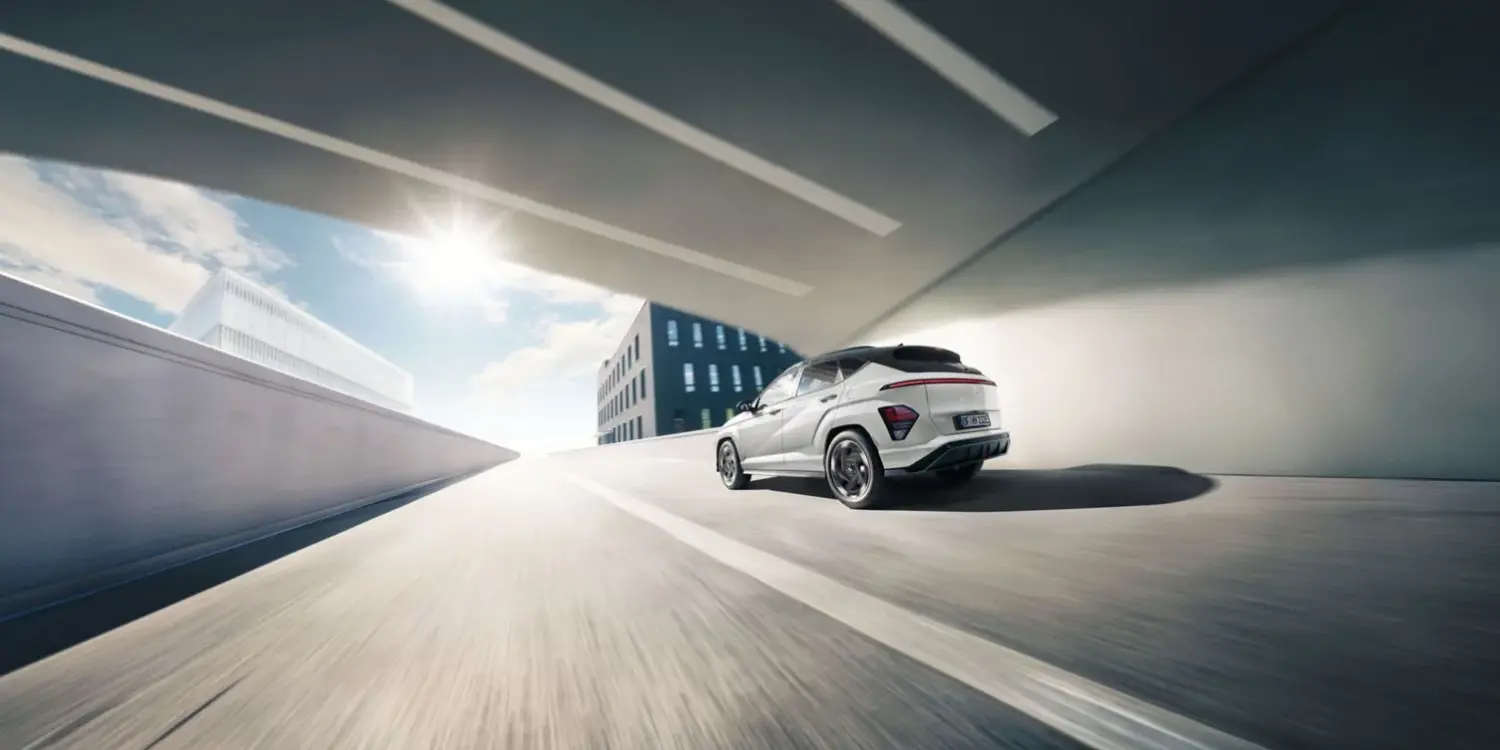 Heckansicht eines weißen Hyundai KONA Elektro, der auf einer städtischen Straße unter einer Brücke fährt.