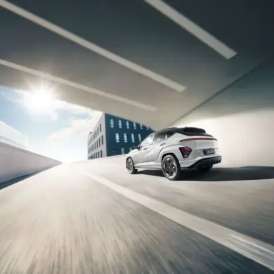 Heckansicht eines weißen Hyundai KONA Elektro, der auf einer städtischen Straße unter einer Brücke fährt.
