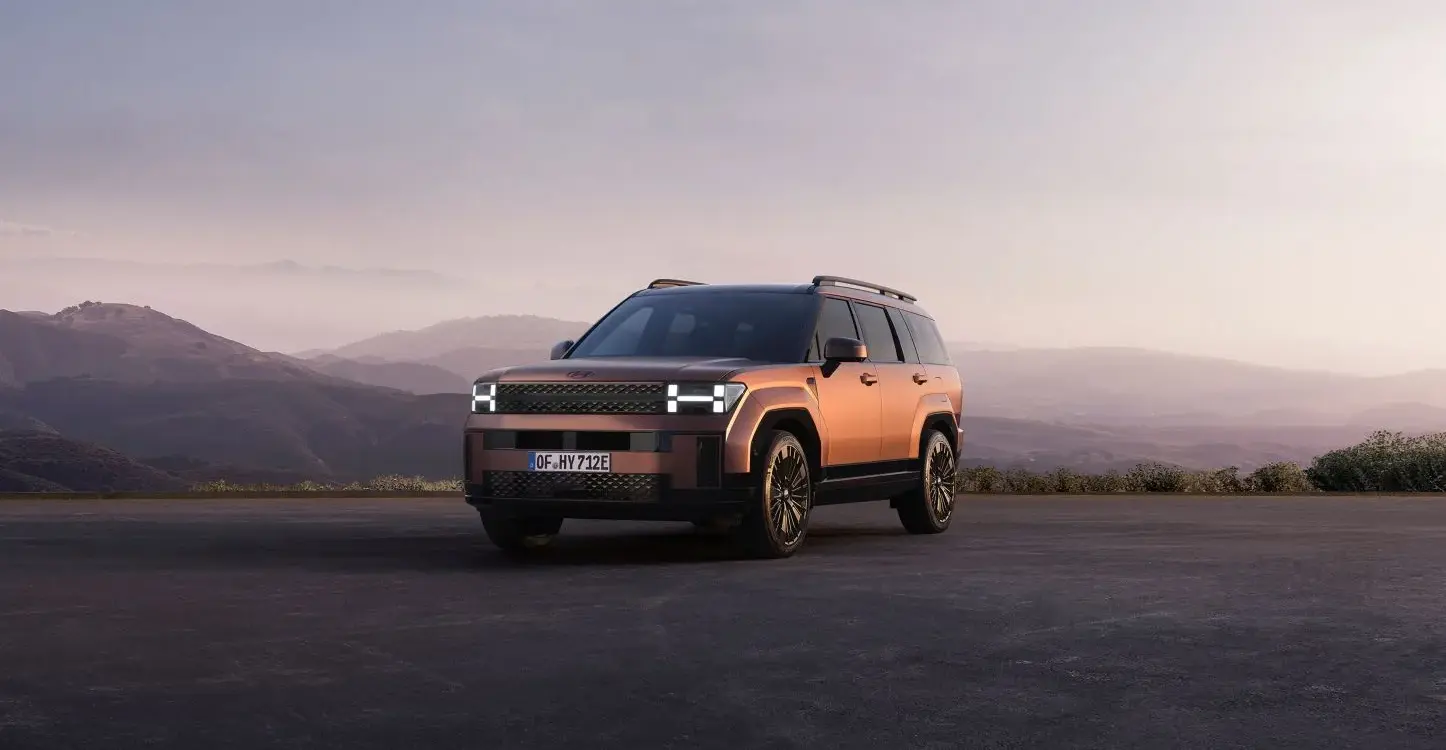 Hyundai Santa Fe Plug-in-Hybrid SUV in kupferfarbener Lackierung steht vor einer malerischen Berglandschaft bei Sonnenuntergang.