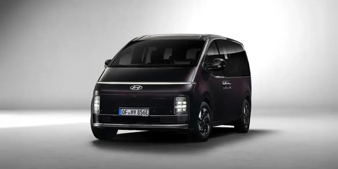 Hyundai STARIA Hybrid in dunkler Lackierung, aufgenommen aus leichtem Winkel von vorne vor neutralem Hintergrund.