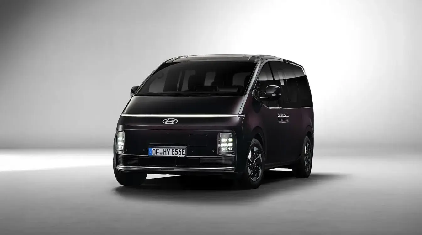 Hyundai STARIA Hybrid in dunkler Lackierung, aufgenommen aus leichtem Winkel von vorne vor neutralem Hintergrund.