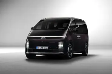 Hyundai STARIA Hybrid in dunkler Lackierung, aufgenommen aus leichtem Winkel von vorne vor neutralem Hintergrund.