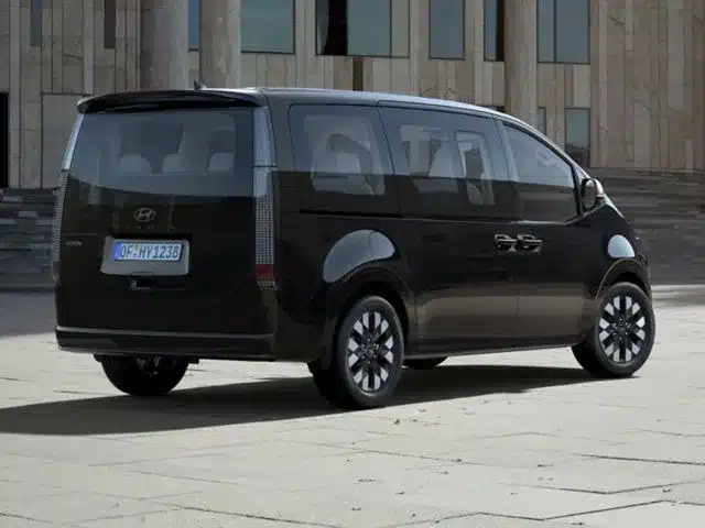 Heckansicht des Hyundai STARIA Hybrid Vans in Schwarz vor einem Gebäude