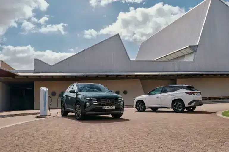 Zwei Hyundai Tucson Plug-in-Hybrid SUV, einer ladend an einer Ladesäule, vor einem modernen Gebäude.