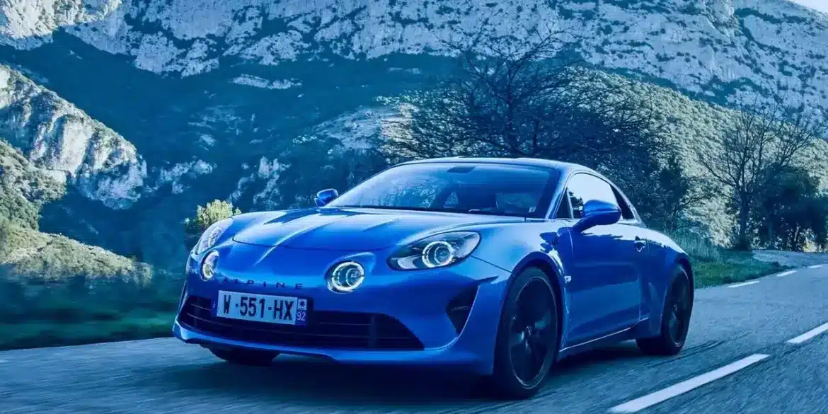 Blauer Alpine A110 fährt auf einer Landstraße vor Bergkulisse.
