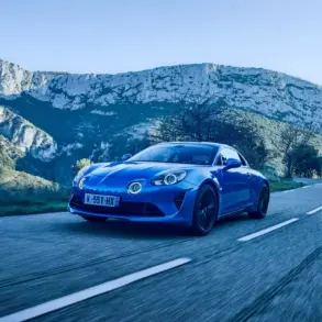 Blauer Alpine A110 fährt auf einer Landstraße vor Bergkulisse.