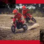 Zwei Kinder fahren die rote GASGAS MC-E 3 2024 auf einer Offroad-Strecke.