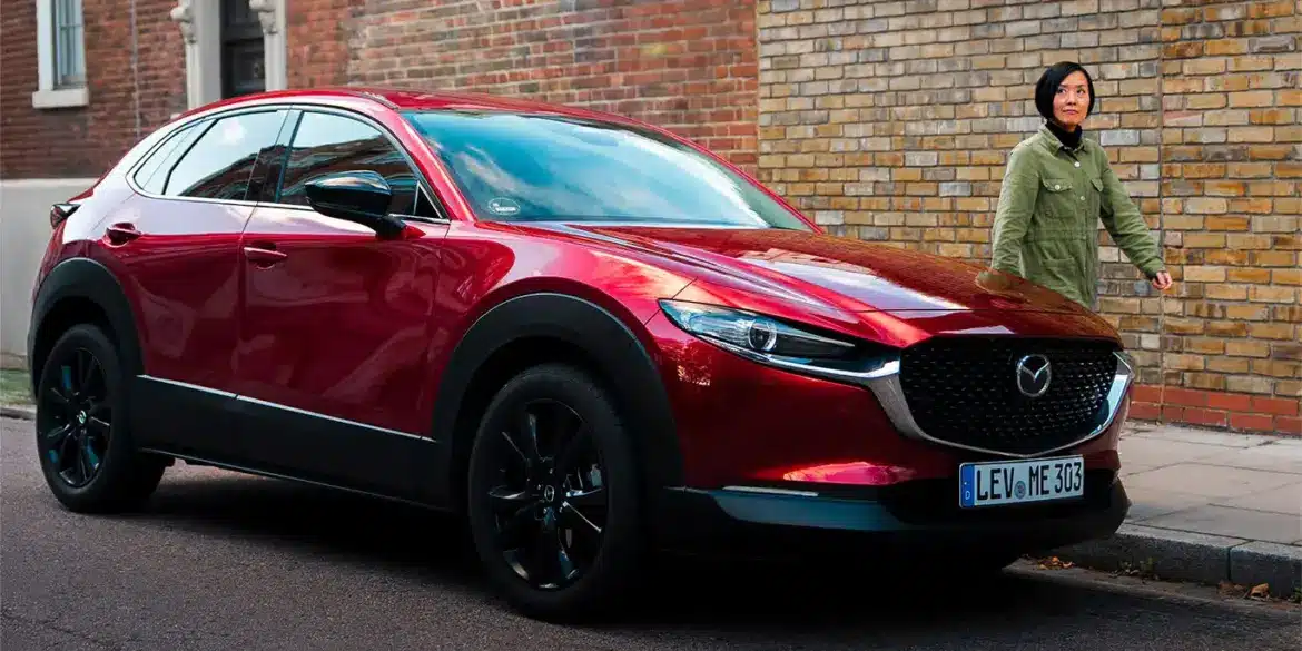 Roter Mazda CX-30 parkt am Straßenrand vor einer Ziegelwand, eine Person geht auf dem Gehweg vorbei