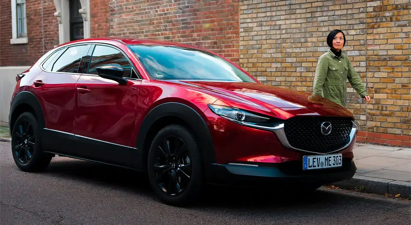Roter Mazda CX-30 parkt am Straßenrand vor einer Ziegelwand, eine Person geht auf dem Gehweg vorbei