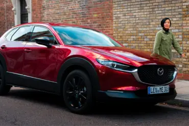 Roter Mazda CX-30 parkt am Straßenrand vor einer Ziegelwand, eine Person geht auf dem Gehweg vorbei