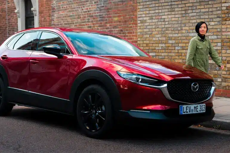 Roter Mazda CX-30 parkt am Straßenrand vor einer Ziegelwand, eine Person geht auf dem Gehweg vorbei