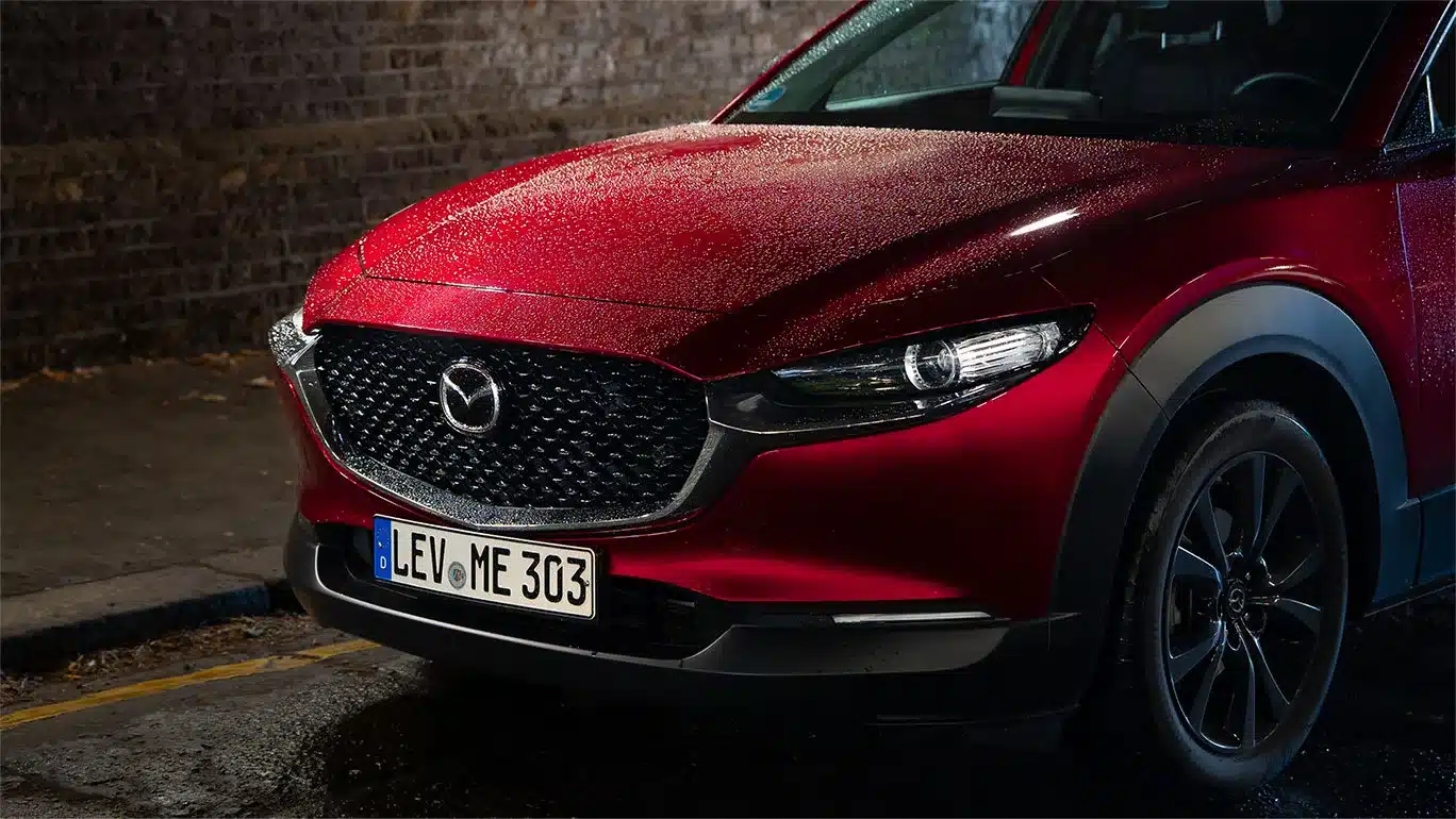 Rote Mazda CX-30 Front im Regen bei Nachtaufnahme, Scheinwerfer und Kühlergrill hervorgehoben