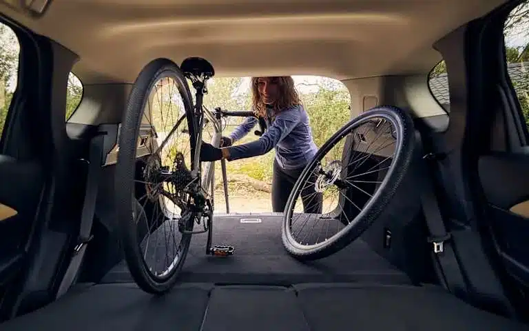 Blick in den Kofferraum eines Mazda CX-5 mit einem eingeladenen Fahrrad, eine Frau lädt Gepäck ein.