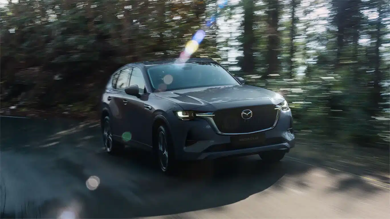 Mazda CX-60 SUV Modelljahr 2026 fährt auf einer nassen Straße im Wald.