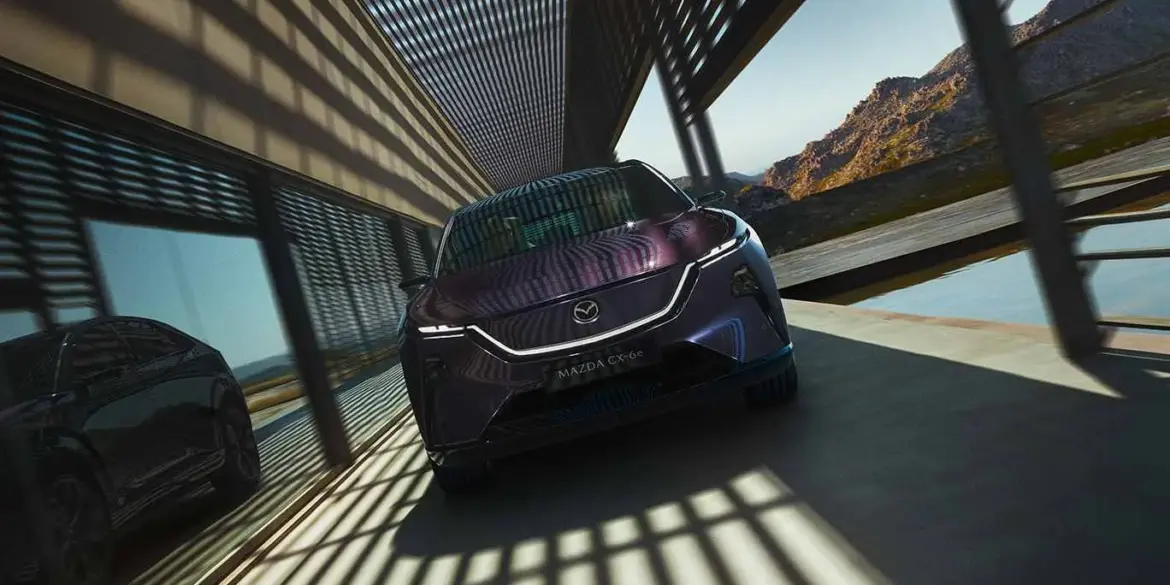 Mazda CX-6e von vorne vor modernen Gebäudestrukturen mit Schattenwurf.