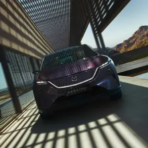 Mazda CX-6e von vorne vor modernen Gebäudestrukturen mit Schattenwurf.