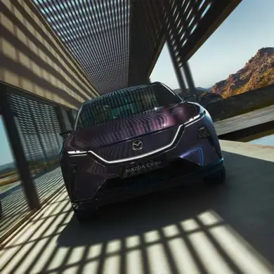 Mazda CX-6e von vorne vor modernen Gebäudestrukturen mit Schattenwurf.