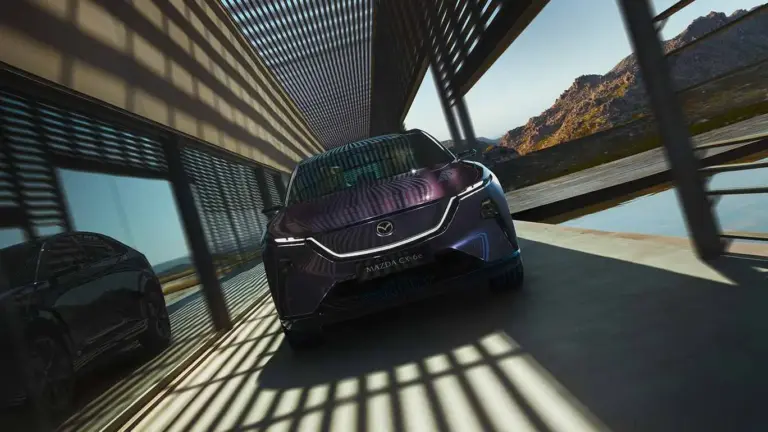 Mazda CX-6e von vorne vor modernen Gebäudestrukturen mit Schattenwurf.