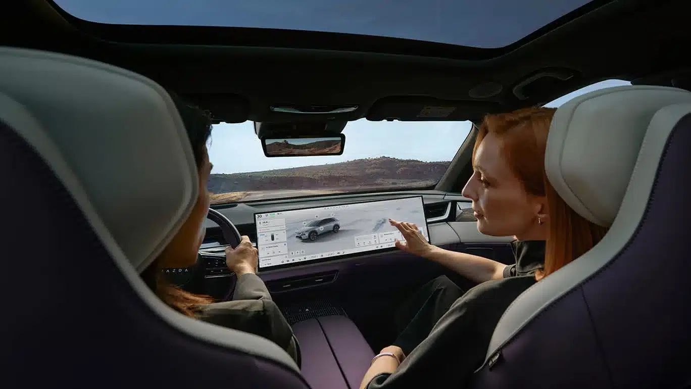 Blick auf das Cockpit des Mazda CX-6e mit großem Touchdisplay und zwei Personen im Vordergrund.