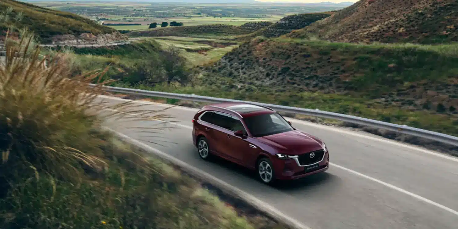 Mazda CX-80 in Rot fährt auf einer Landstraße durch hügelige Landschaft