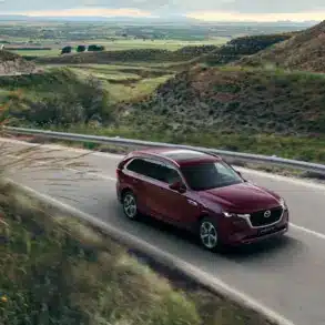 Mazda CX-80 in Rot fährt auf einer Landstraße durch hügelige Landschaft