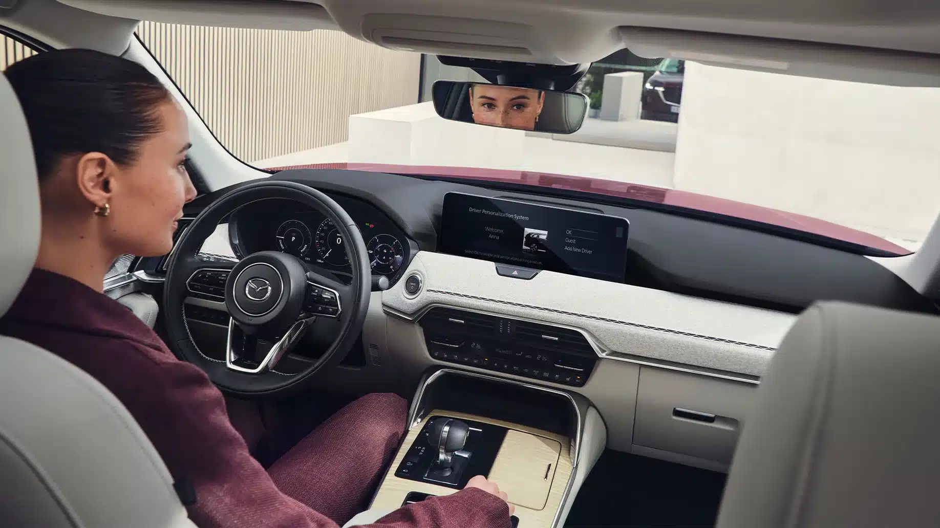 Innenraum des Mazda CX-80 mit Blick auf das Lenkrad, das zentrale Display und eine Fahrerin.