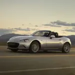 Mazda MX-5 2024 Roadster in Silber fährt bei Sonnenuntergang über eine Landstraße