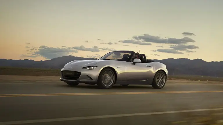 Mazda MX-5 2024 Roadster in Silber fährt bei Sonnenuntergang über eine Landstraße