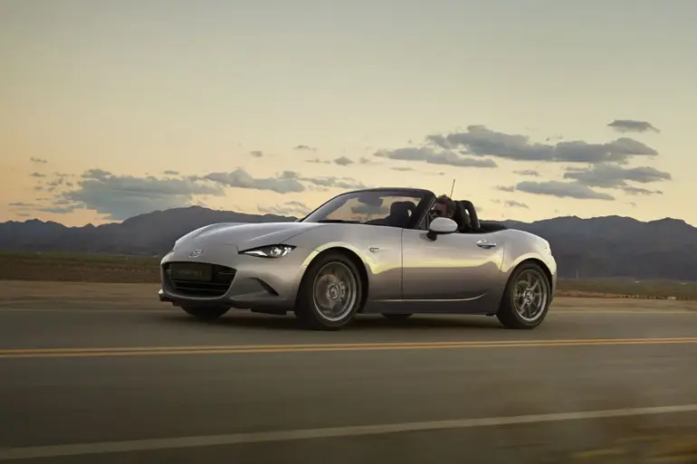 Mazda MX-5 2024 Roadster in Silber fährt bei Sonnenuntergang über eine Landstraße