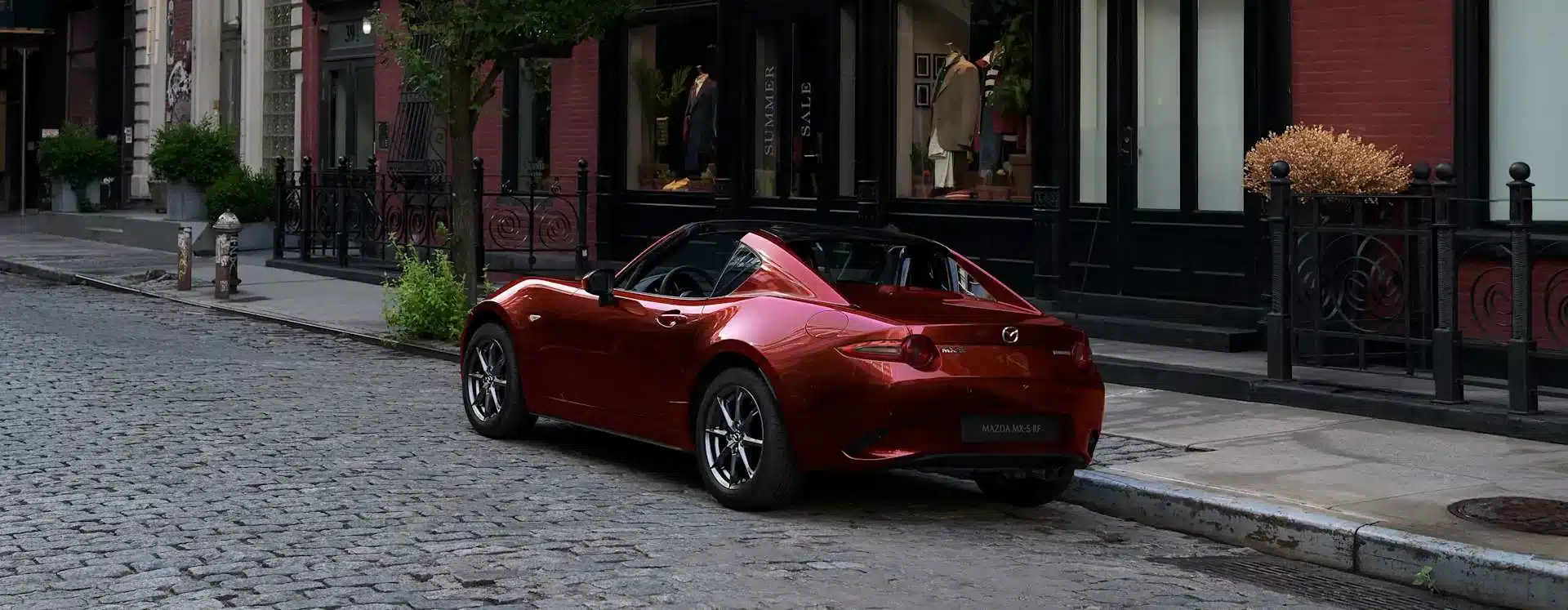 Mazda MX-5 RF mit geöffnetem Hardtop in Rot auf einer urbanen Straße geparkt.