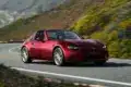 Roter Mazda MX-5 RF fährt auf einer kurvenreichen Straße entlang einer malerischen Landschaft.