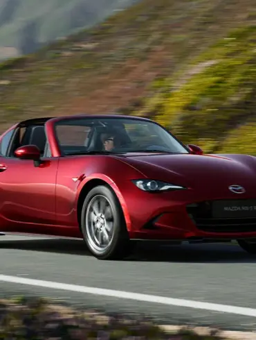 Roter Mazda MX-5 RF fährt auf einer kurvenreichen Straße entlang einer malerischen Landschaft.