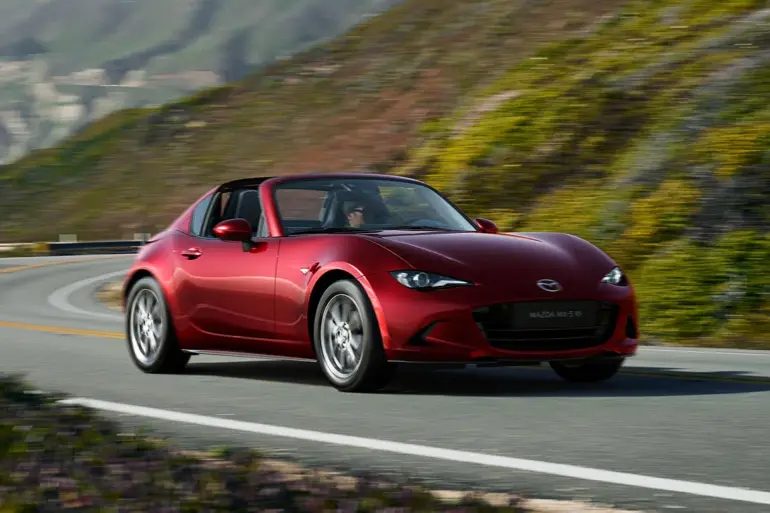 Roter Mazda MX-5 RF fährt auf einer kurvenreichen Straße entlang einer malerischen Landschaft.