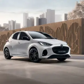 Mazda2 Hybrid 2024 in Weiß fährt auf einer urbanen Straße vor moderner Kulisse.