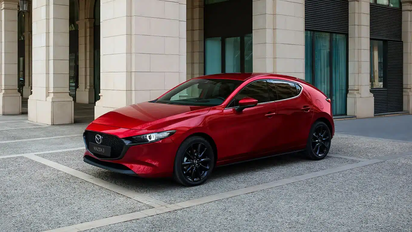 Roter Mazda3 Fünftürer Modelljahr 2024 geparkt vor einem Gebäude mit Säulen.