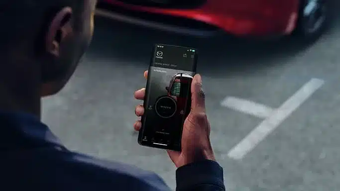 Person nutzt die Mazda-App auf dem Smartphone neben einem geparkten Mazda3.