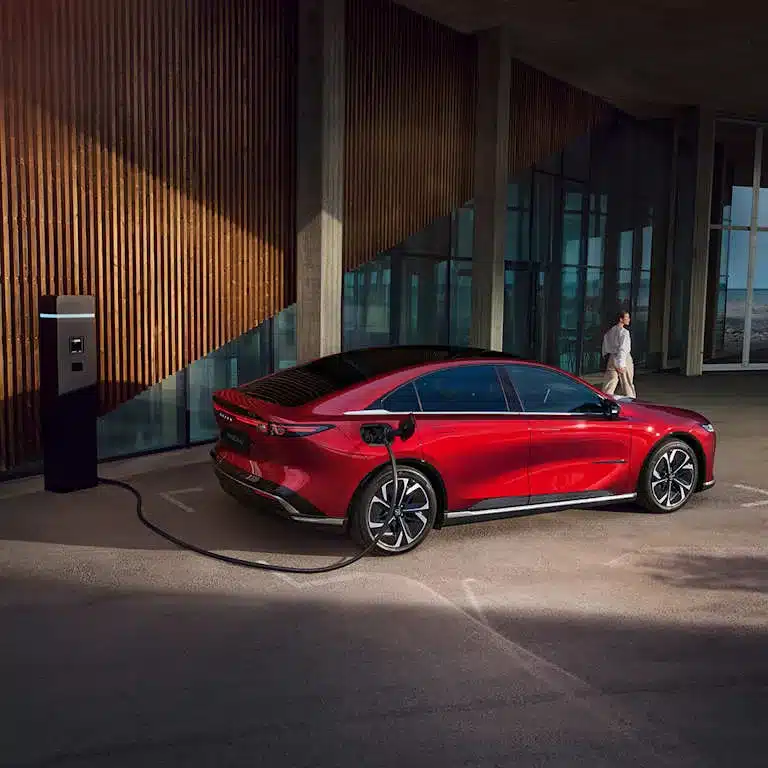 Roter Mazda6e Liftback an einer Ladesäule vor einem modernen Gebäude.