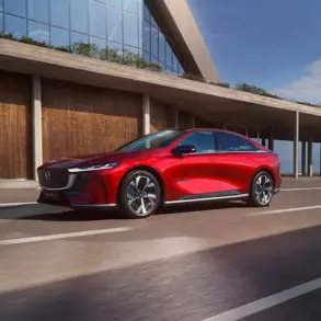 Rote Mazda6e vollelektrische Limousine fährt auf einer modernen Straße vor einem Gebäude.