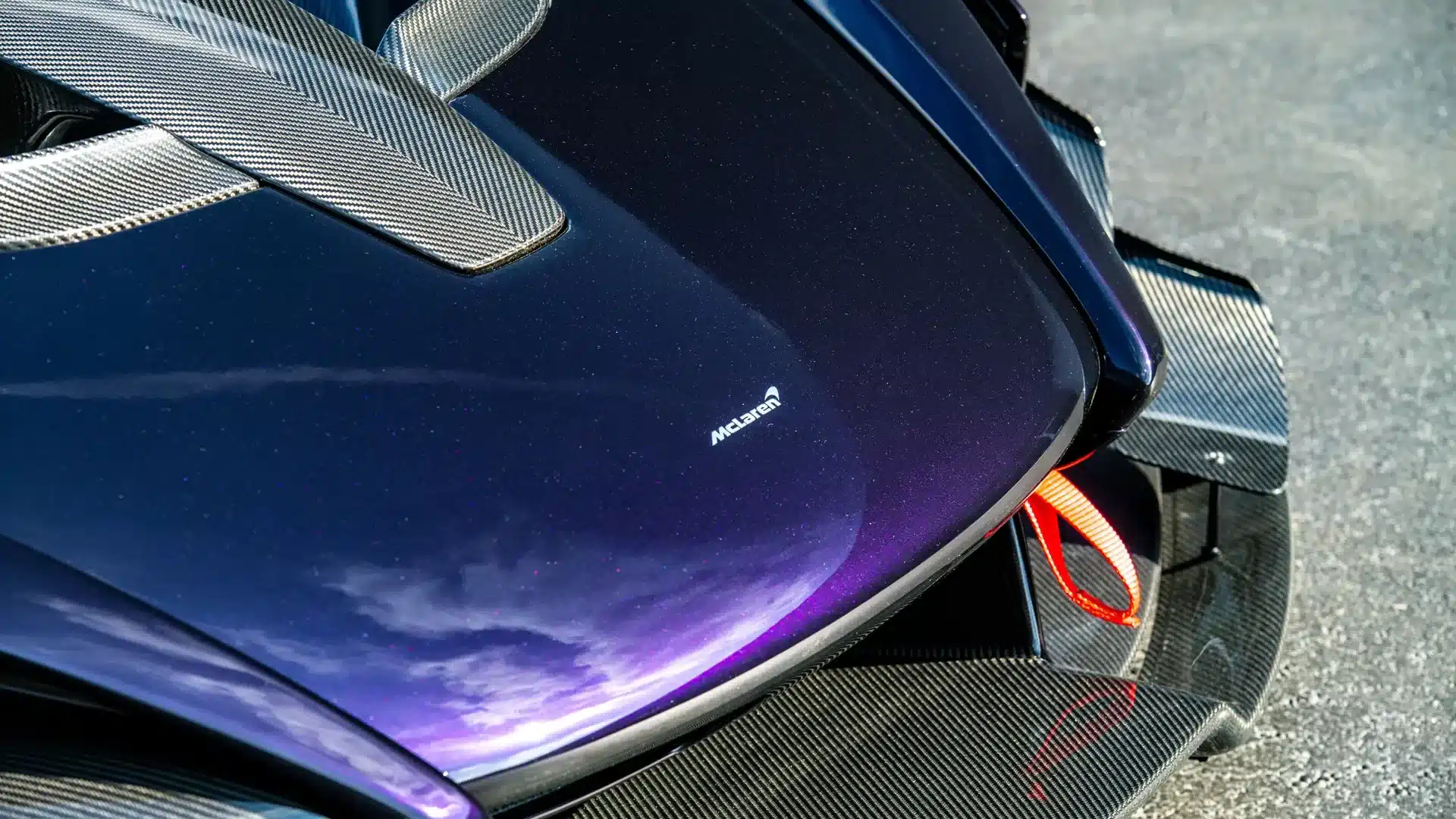 Makroaufnahme der Motorhaube des McLaren Senna GTR in Amethyst Black mit sichtbaren Carbonfaser-Elementen und McLaren-Logo