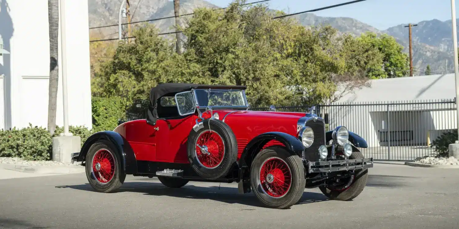 Stutz Model BB Custom Black Hawk Two-Passenger Speedster von 1928 in Rot und Schwarz auf einer Straße, Cabriolet-Verdeck und klassische Speichenräder.