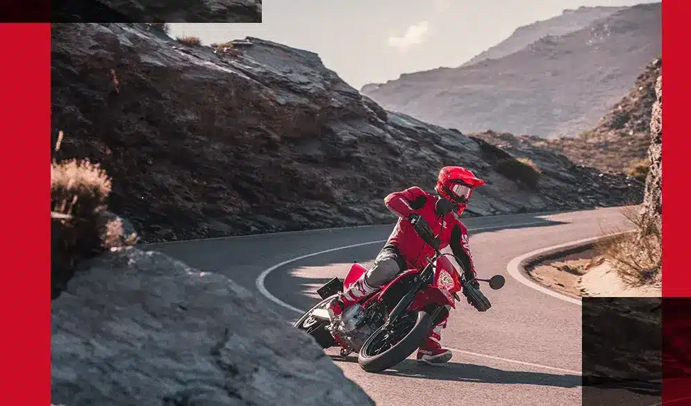 Motorradfahrer auf roter GasGas SM 700 2024 beim sportlichen Fahren auf einer kurvigen Bergstraße.