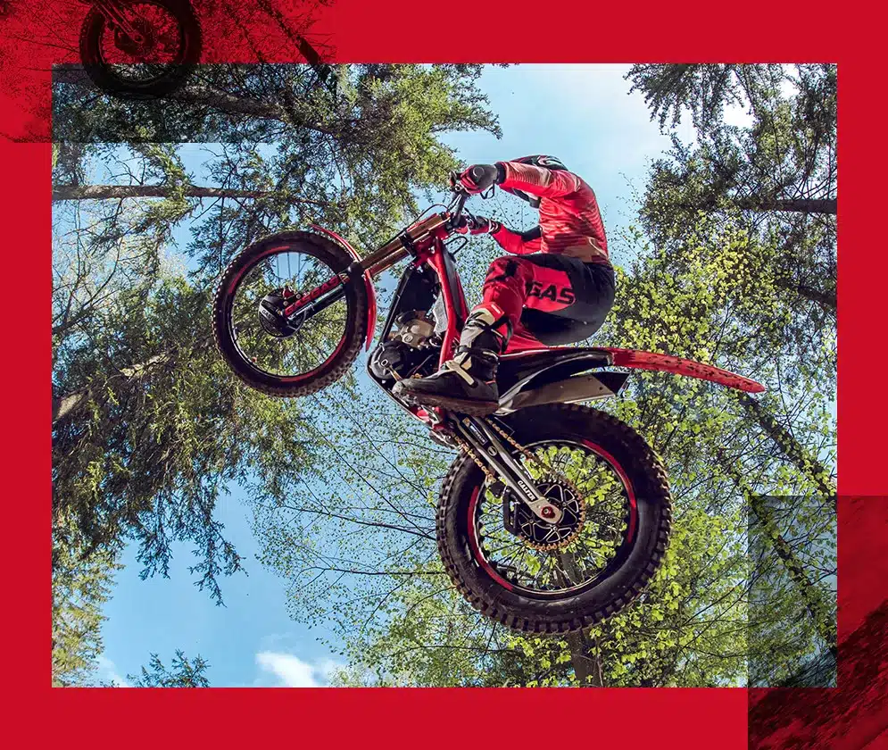 GASGAS TXT GP 250 2025 Motorrad beim Sprung im Trial-Gelände, Fahrer in roter Ausrüstung, umgeben von Bäumen.