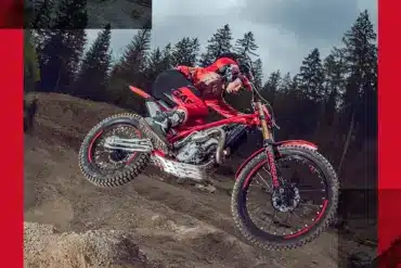 GASGAS TXT GP 250 2025 Trial-Motorrad im Sprung im Gelände, Fahrer mit roter Ausrüstung, Wald im Hintergrund.
