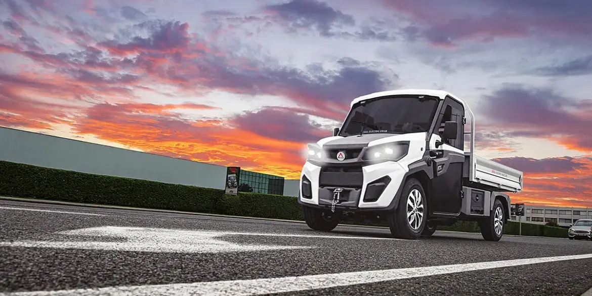 Alkè ATX Elektro-Nutzfahrzeug fährt über eine Straße vor farbigem Himmel.