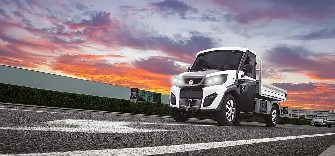 Alkè ATX Elektro-Nutzfahrzeug fährt über eine Straße vor farbigem Himmel.