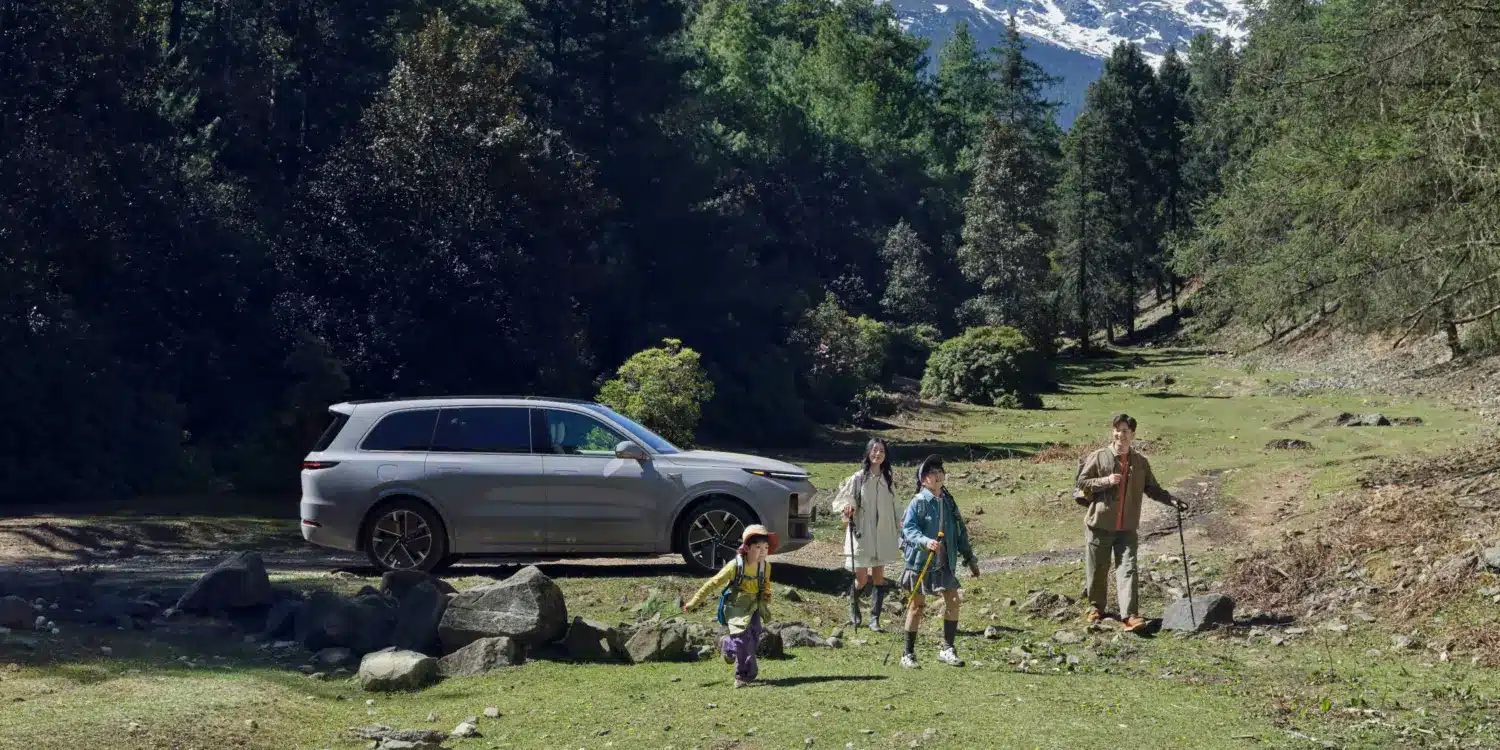 Familie vor einem silbernen Li L9 SUV in einer Waldlandschaft mit Bergen im Hintergrund.
