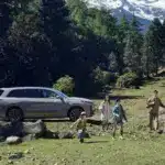 Familie vor einem silbernen Li L9 SUV in einer Waldlandschaft mit Bergen im Hintergrund.