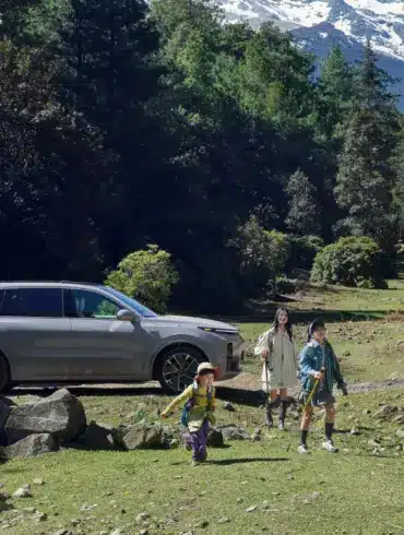 Familie vor einem silbernen Li L9 SUV in einer Waldlandschaft mit Bergen im Hintergrund.